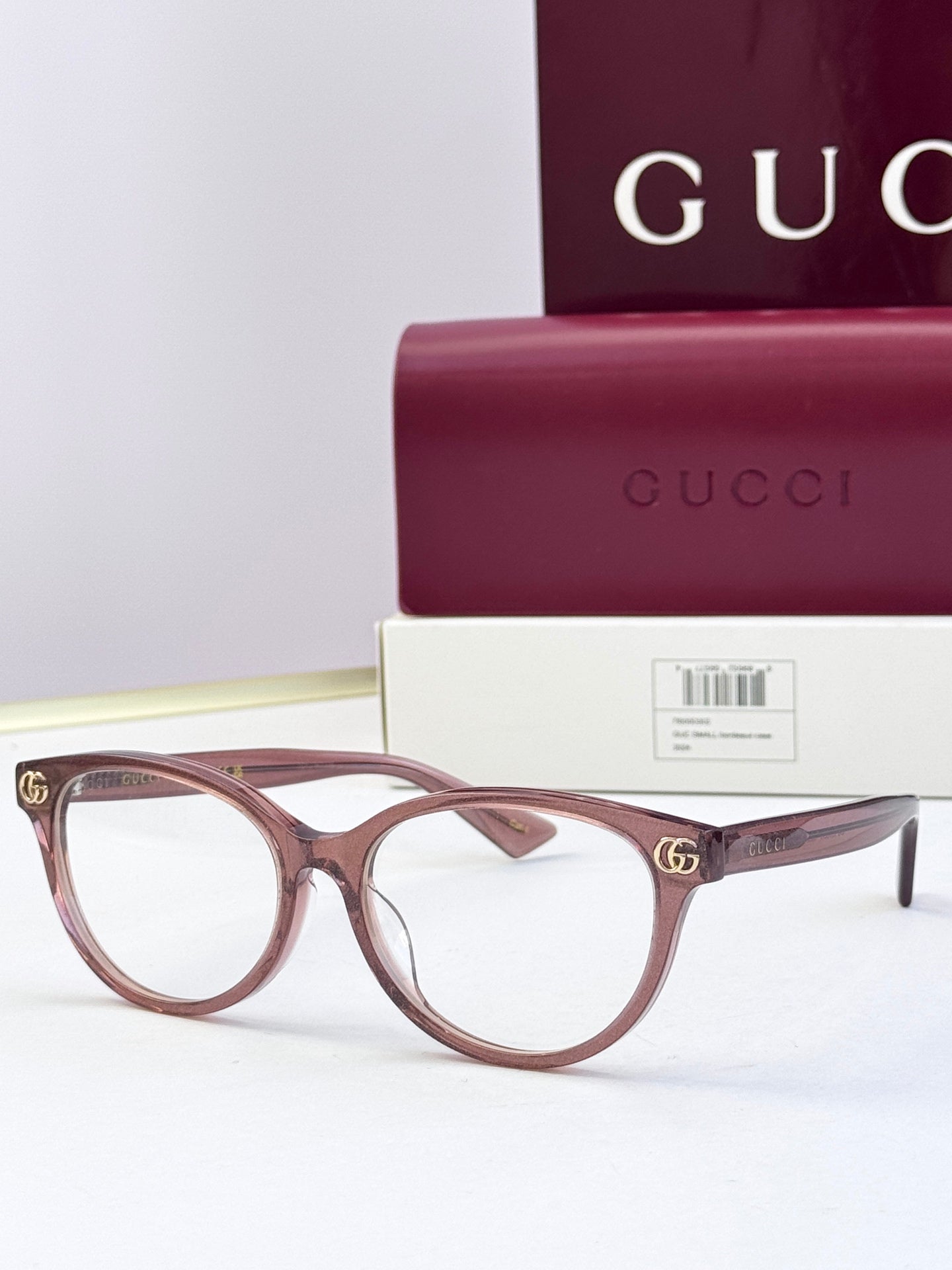 Burgundy eyeglass frames with clear lenses and gold logo detail at temples