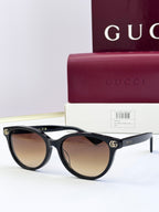 Black eyeglass frames with warm brown lenses and gold logo detail at temples