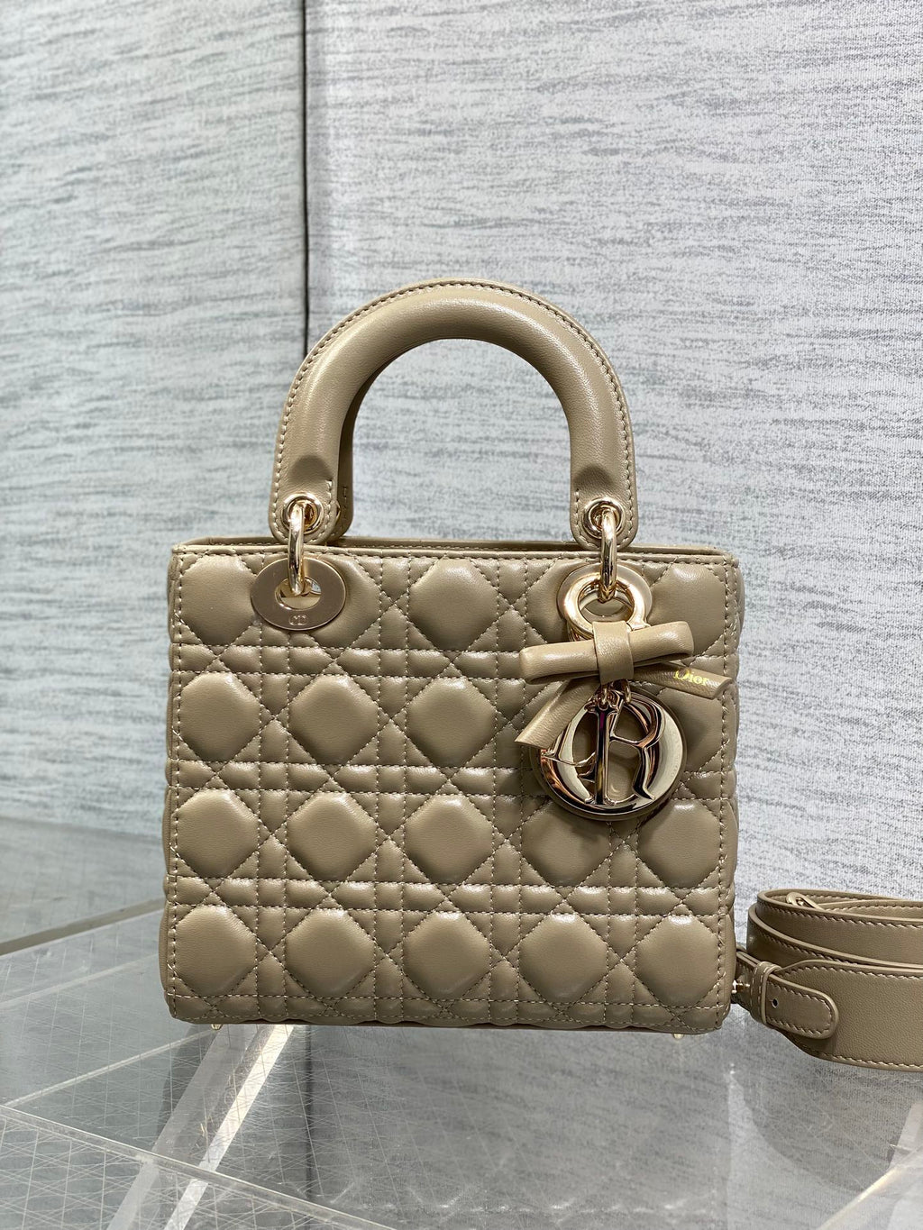 Dior quilted mini handbag in beige with bow charm, gold hardware, and shoulder strap