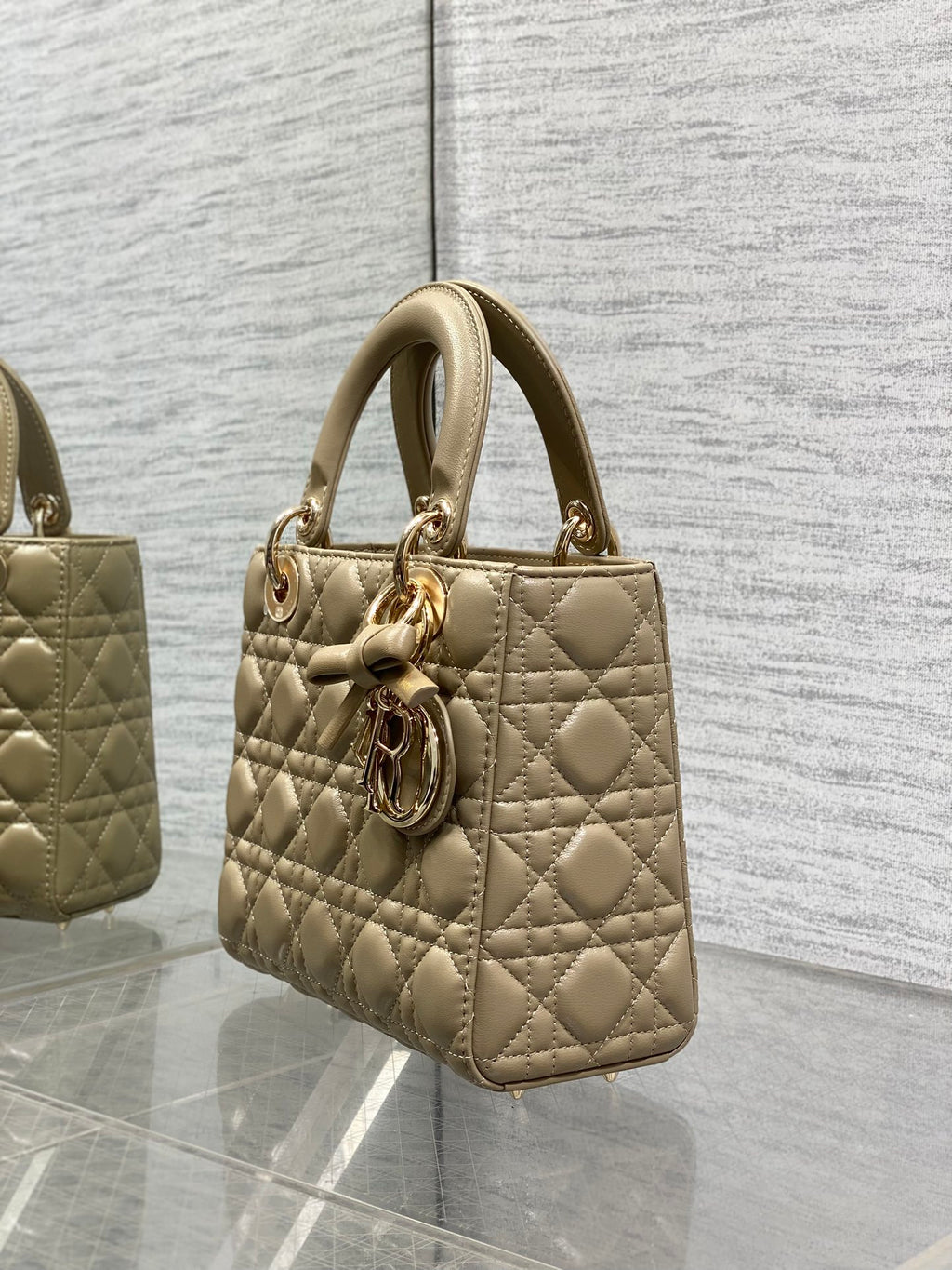 Dior quilted handbag in beige shown from the side with top handle and charm accent