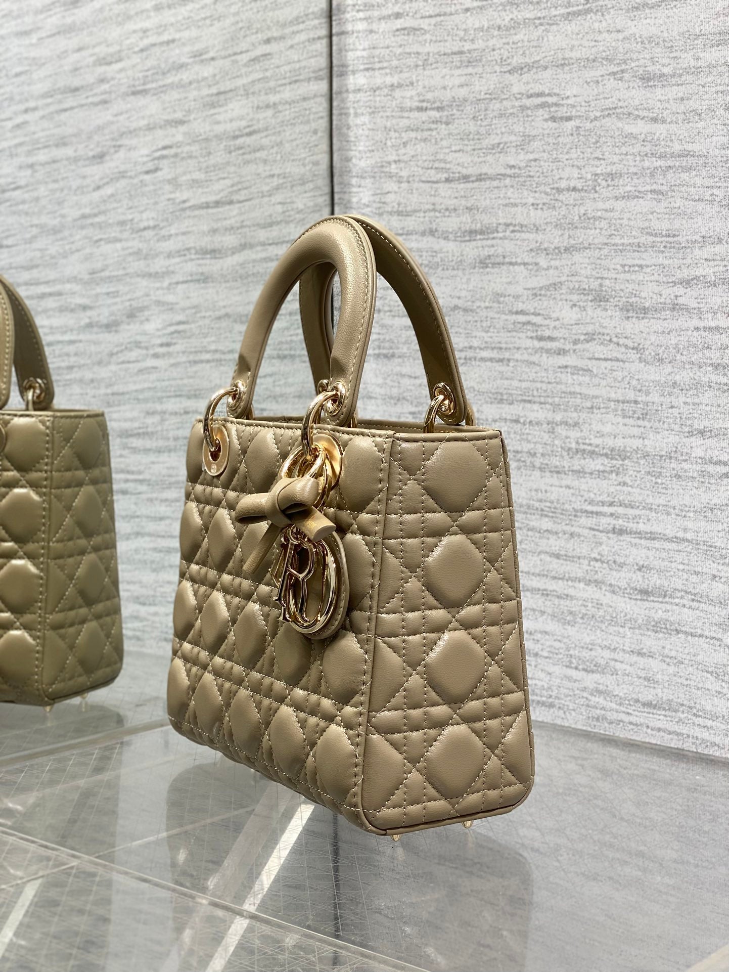 Dior quilted handbag in beige shown from the side with top handle and charm accent