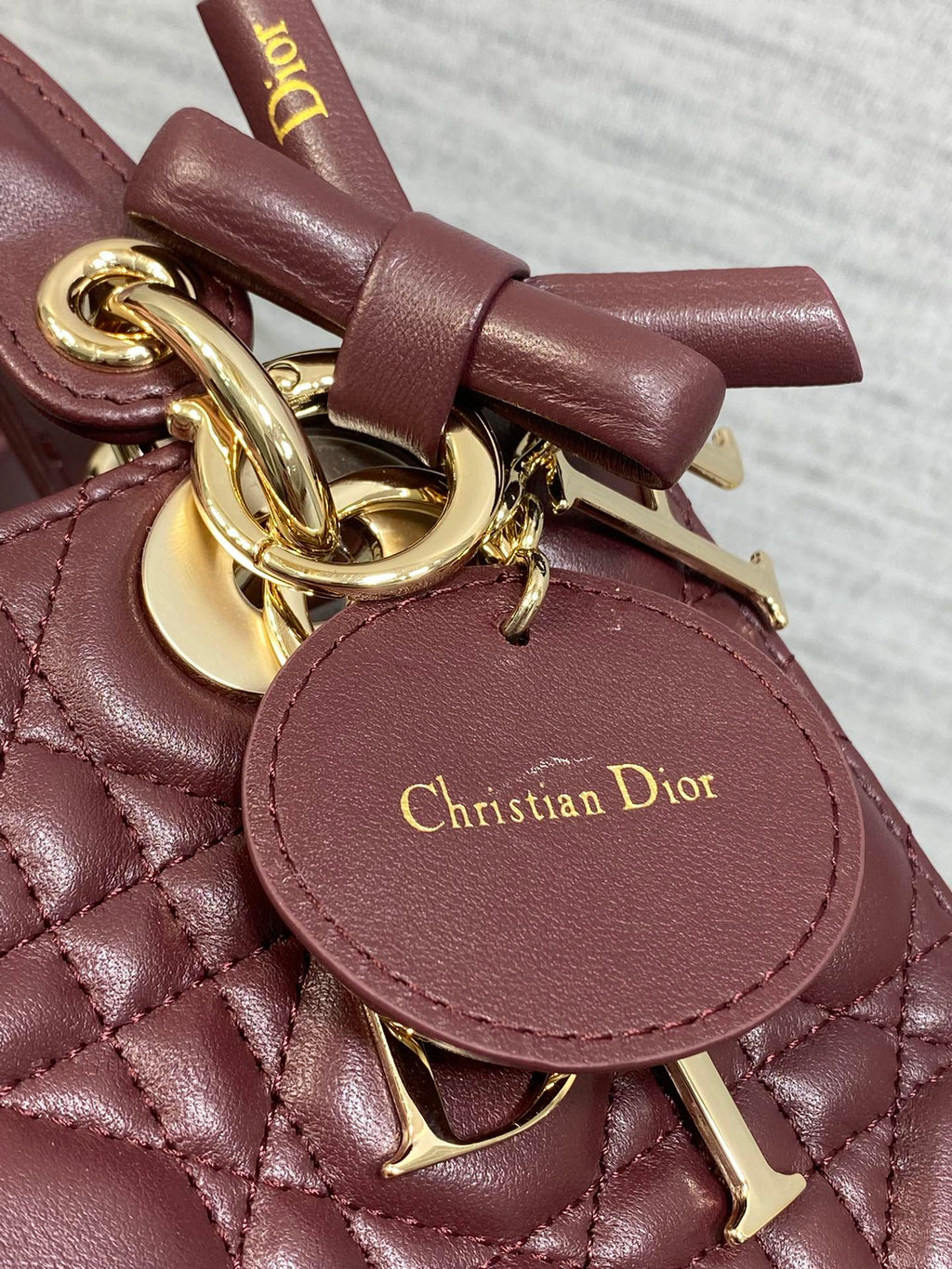 Burgundy leather mini bag with knotted strap, gold charm, and Dior logo tag