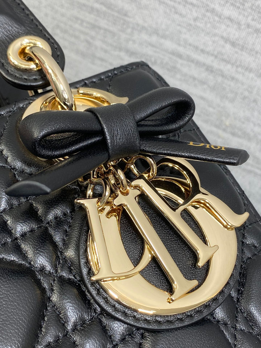 Close-up of black quilted bag with gold-tone Dior logo medallion and bow detail