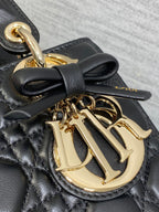 Close-up of black quilted bag with gold-tone Dior logo medallion and bow detail