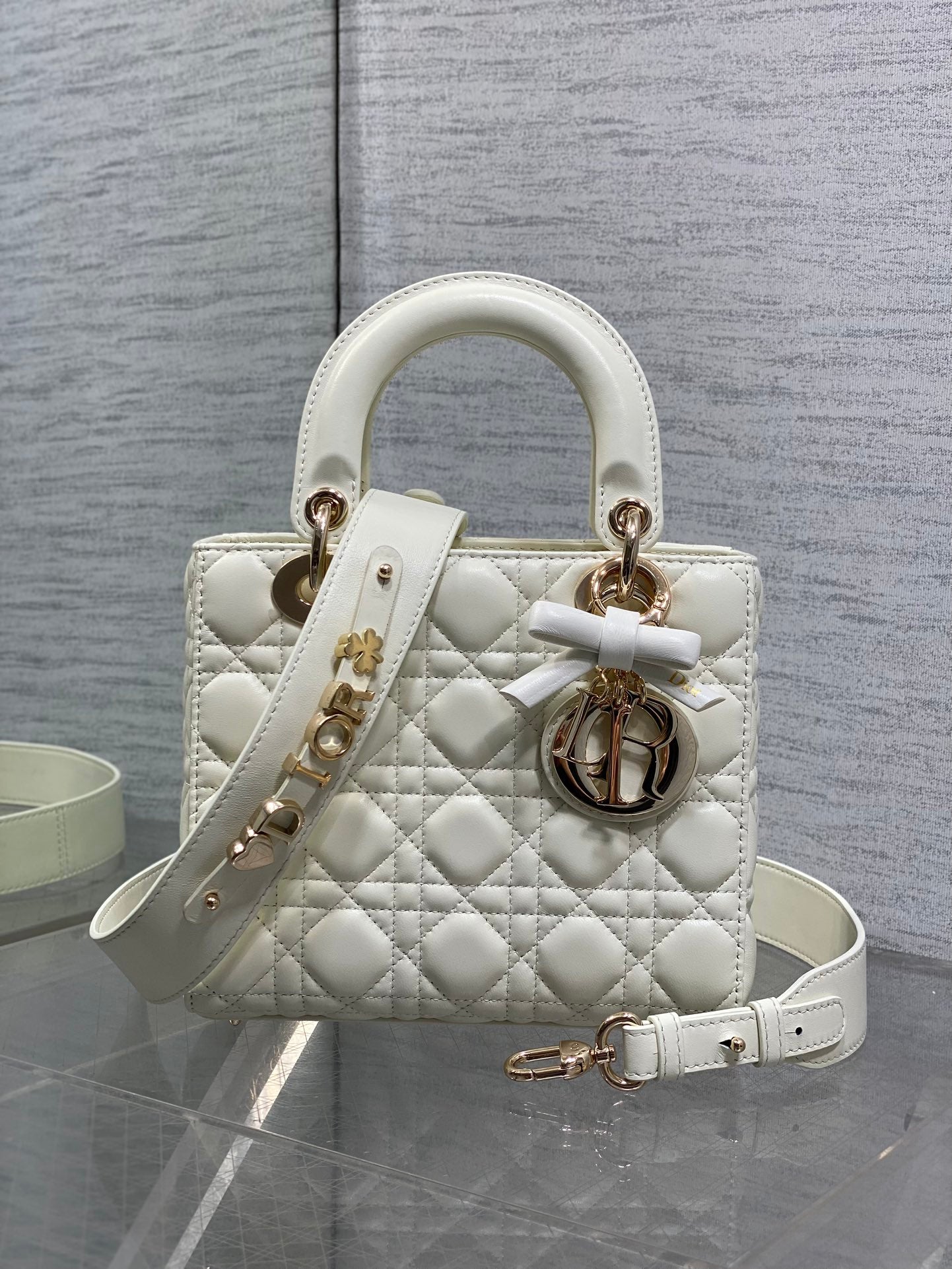 White quilted handbag with top handles, bow strap, and gold-tone Dior charm
