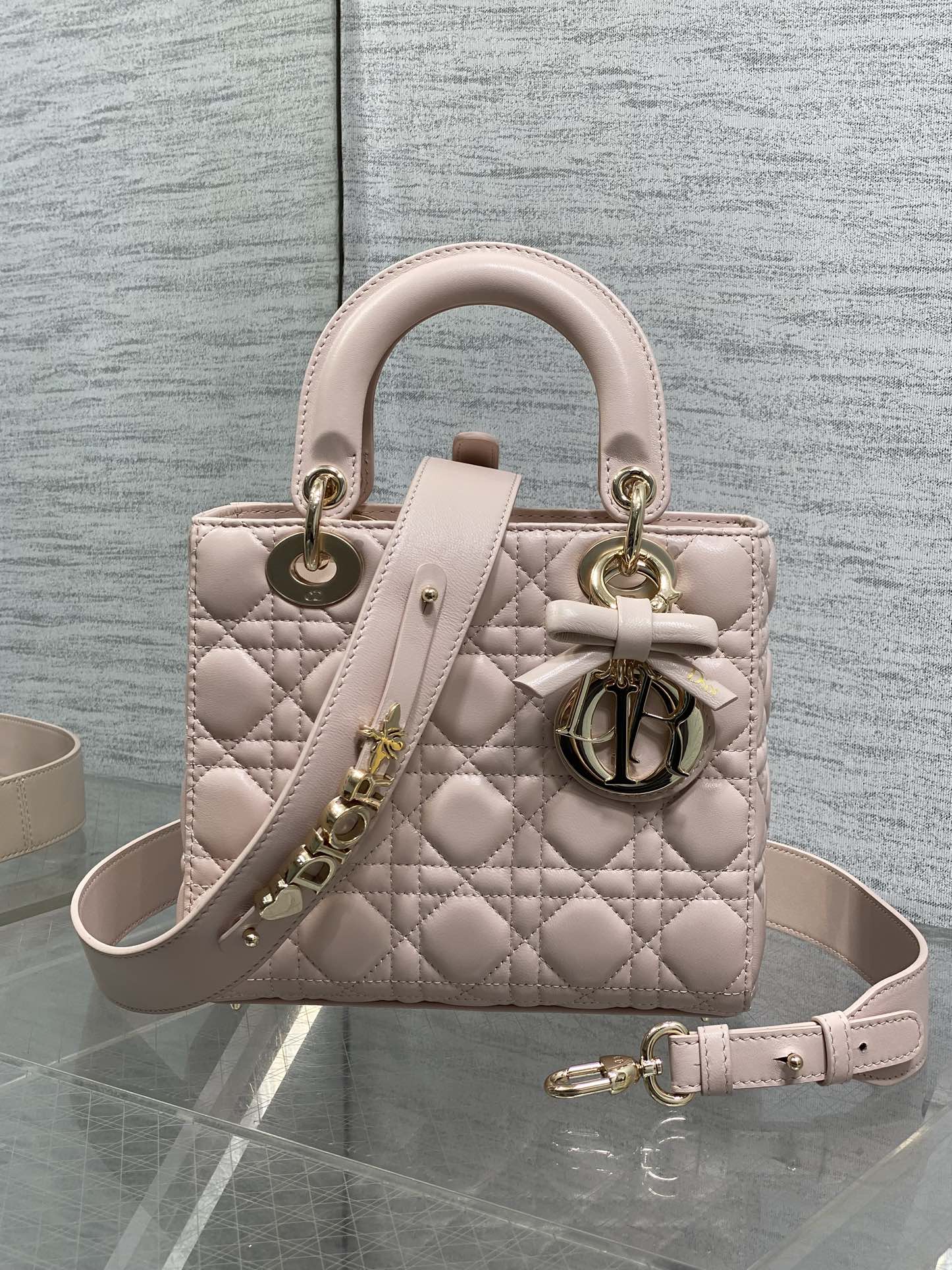 Light pink quilted mini handbag with top handles, bow detail, and shoulder strap