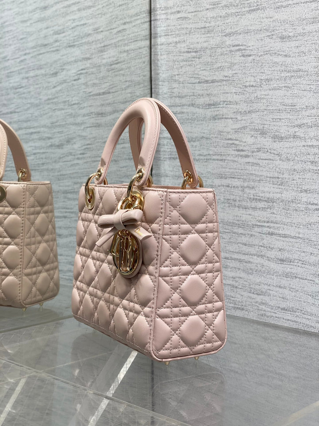 Light pink quilted mini handbag with top handles and gold-tone charm on the front