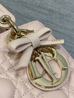 Light pink quilted handbag detail with gold-tone O charm and bow tie on strap