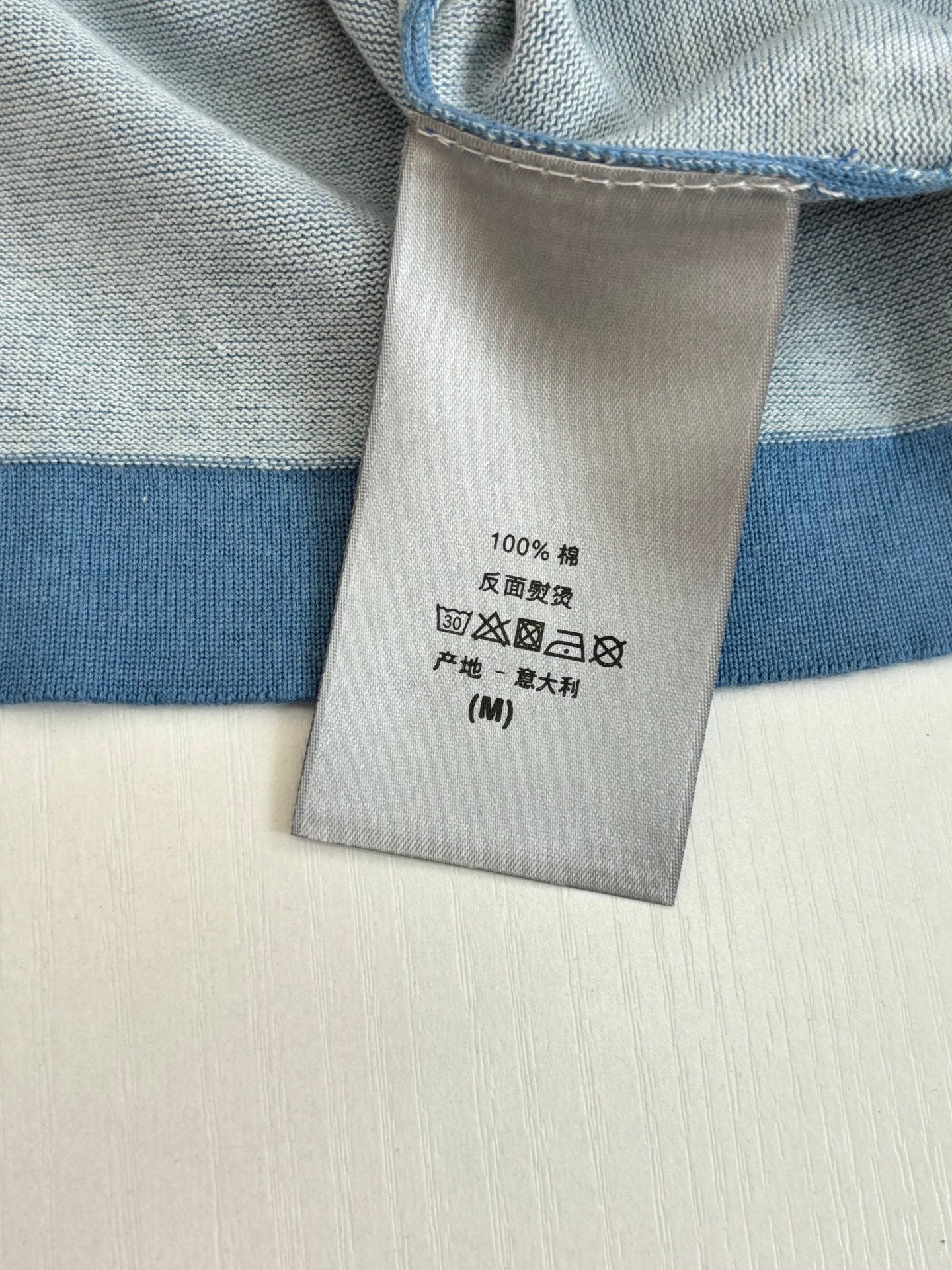 Blue T-shirt care label with 100% cotton and washing symbols