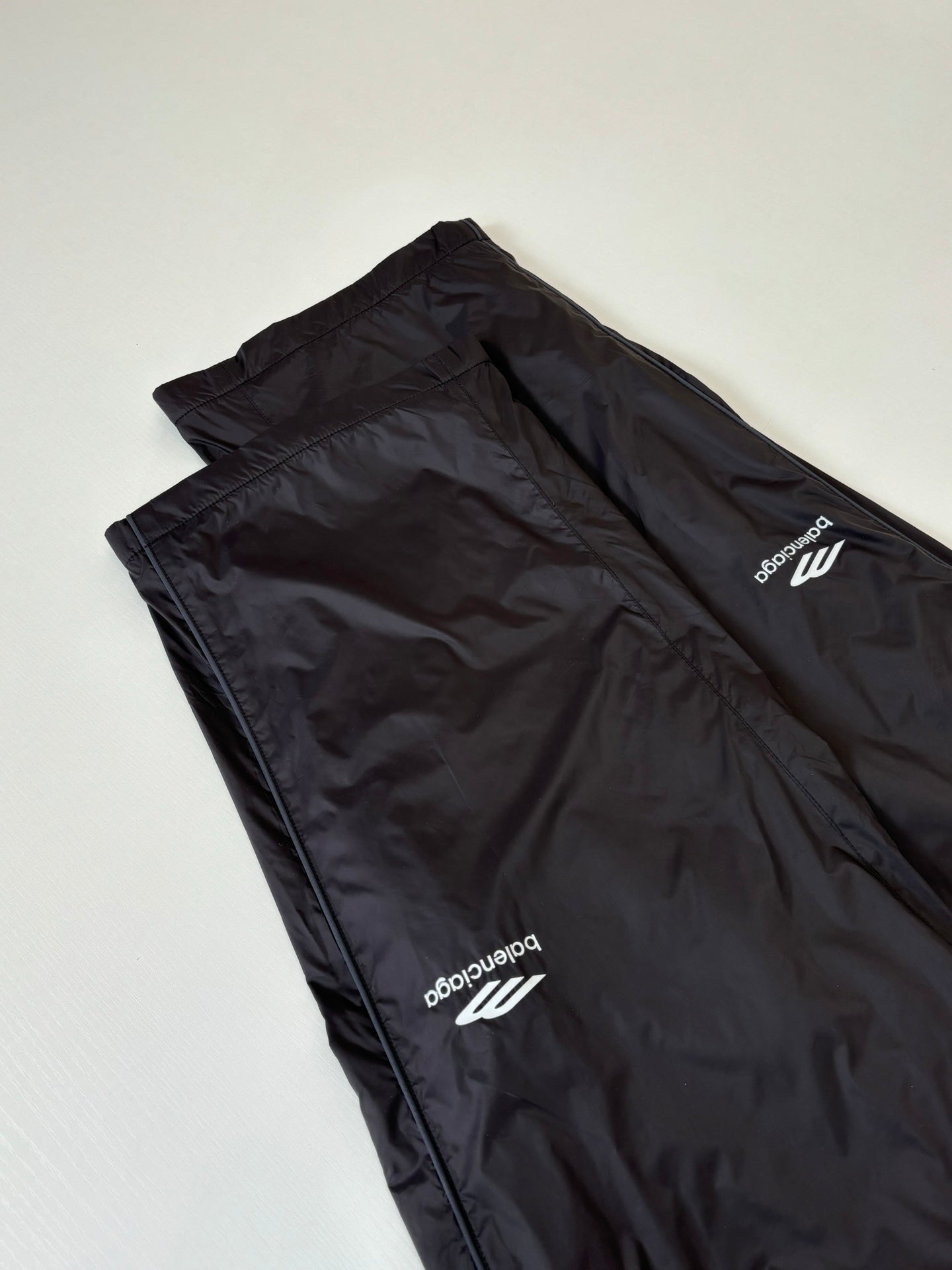 Balenciaga black wide-leg pants folded flat, white logo print on leg