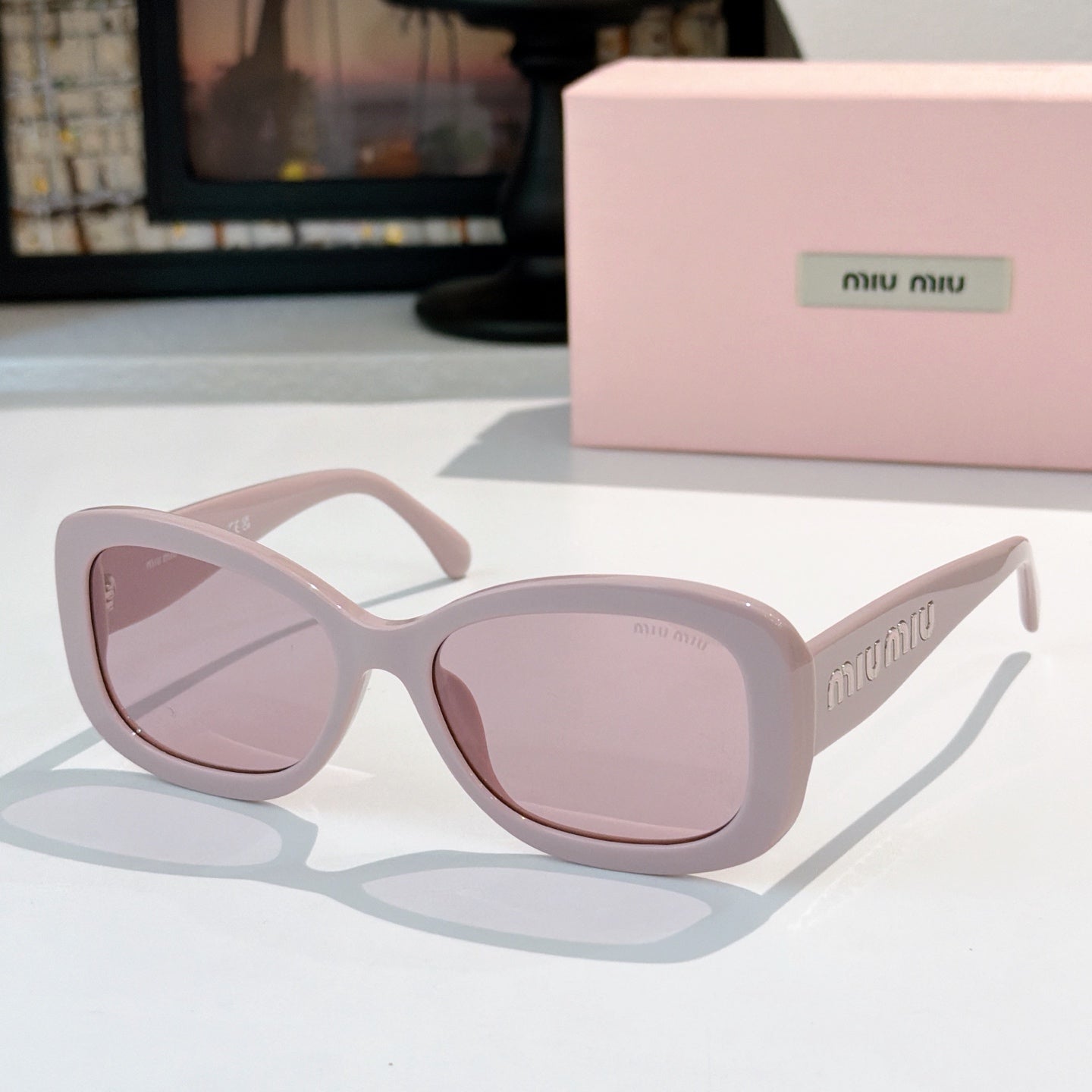 MiuMiu sunglasses with light pink frames and pale rose lenses, cat-eye style.