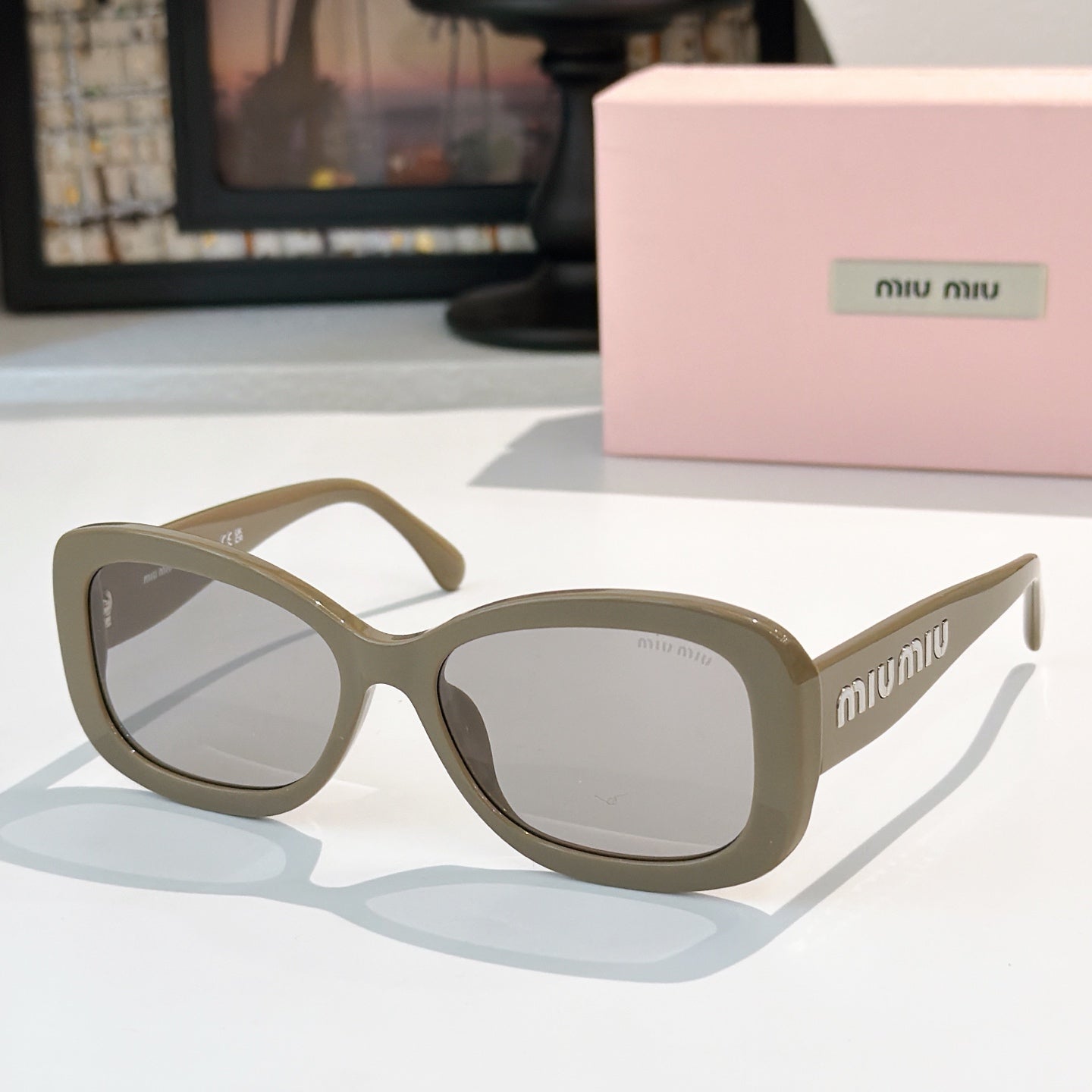 MiuMiu sunglasses with light tan frames and clear gray lenses, cat-eye style.