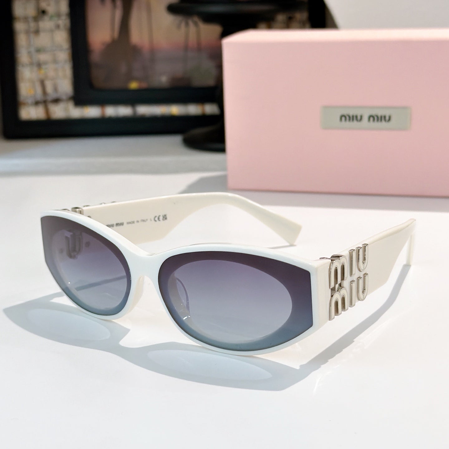 White sunglasses with light blue lenses and gold Miu Miu logo on the temples