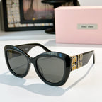 MiuMiu cat-eye sunglasses with dark frames and gray tinted lenses, gold logo side details