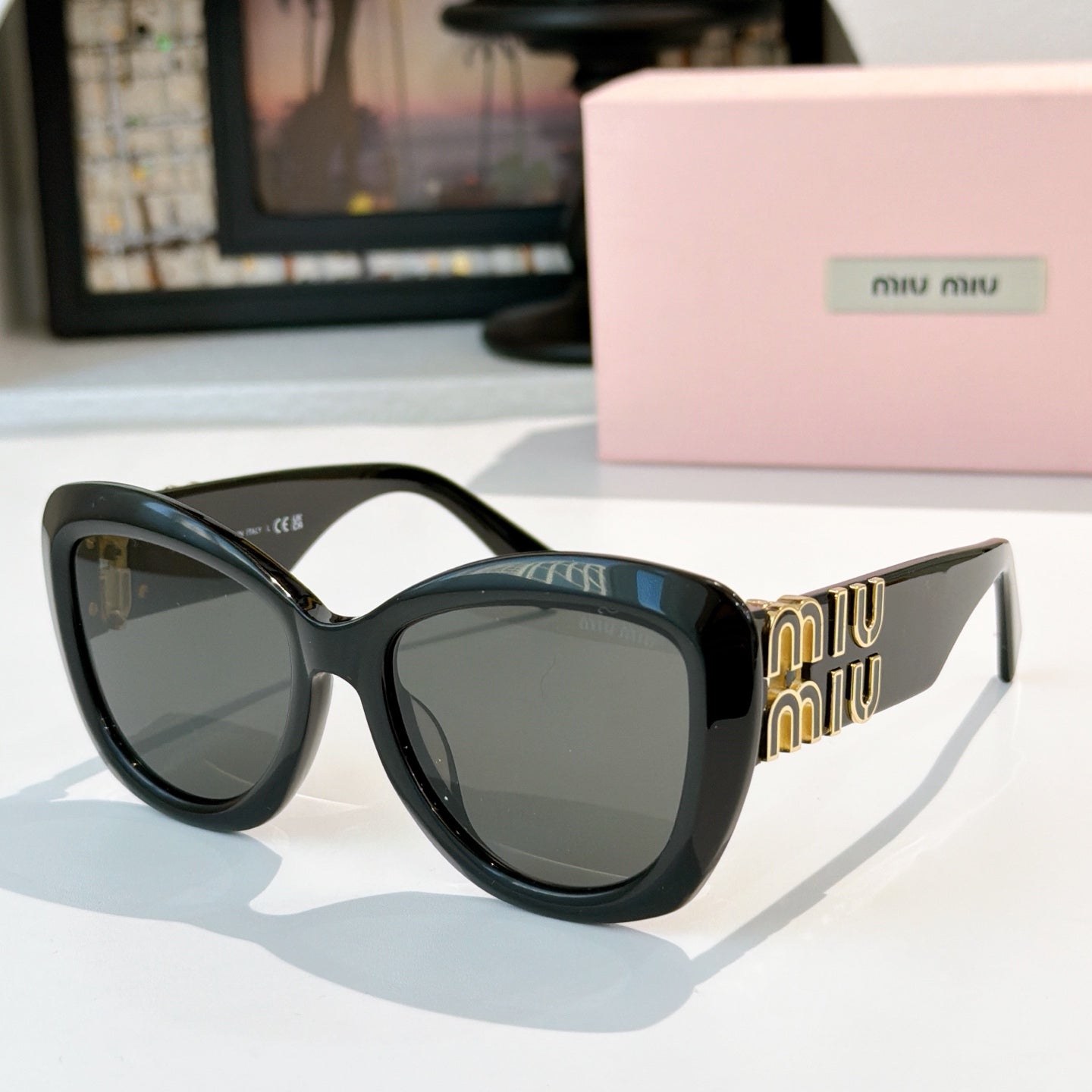 MiuMiu cat-eye sunglasses with dark frames and gray tinted lenses, gold logo side details