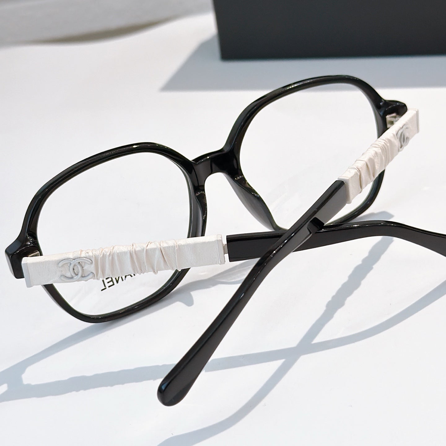 Chanel eyeglasses with black frames and white strap-style temple, clear lenses.