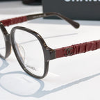 Chanel eyeglasses close-up: dark frame with burgundy ribbed temple and clear lens.