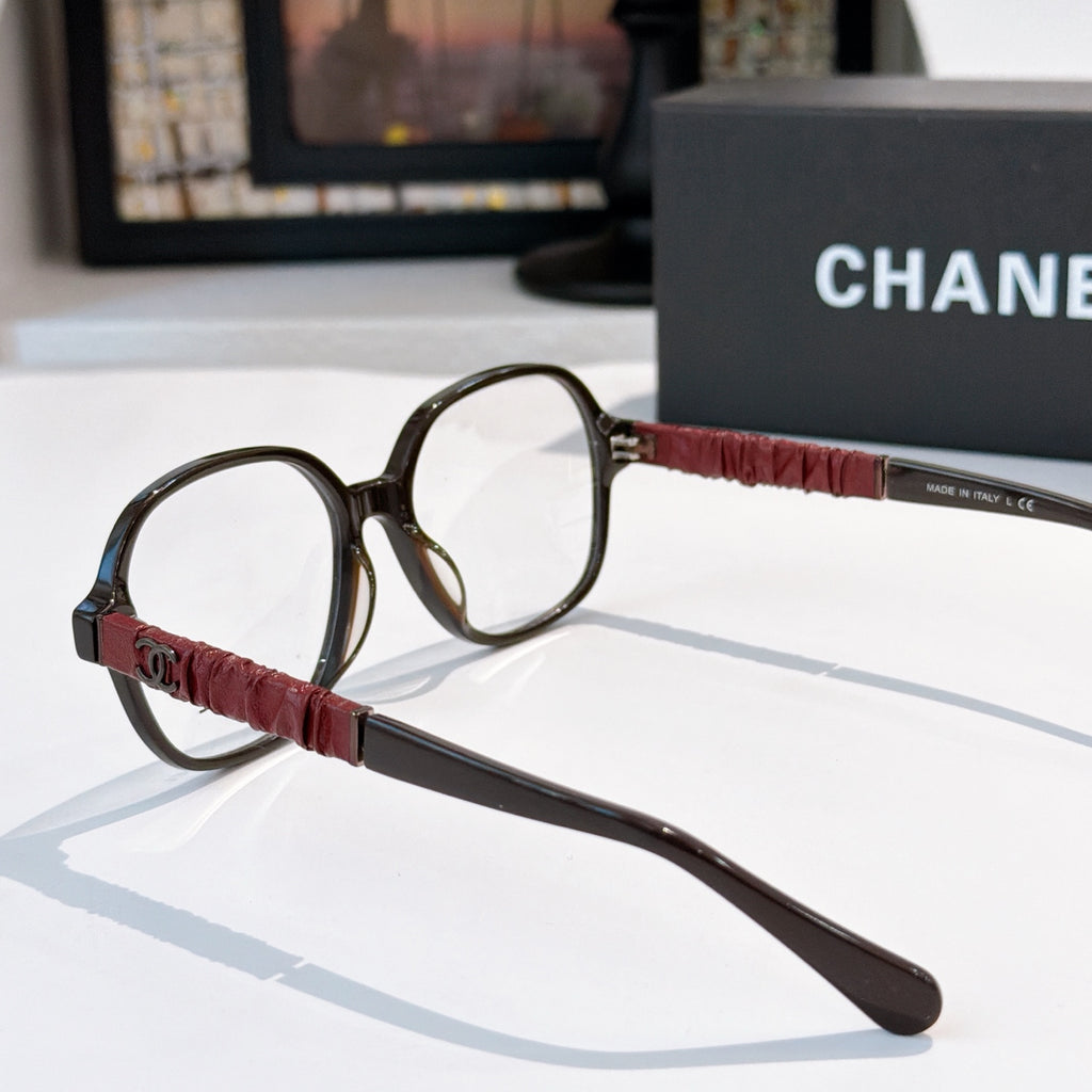 Chanel eyeglasses side view with black frame, burgundy strap-style temple, clear lens.