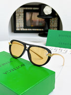 Sunglasses with black frame and gold-tone accents, amber-tinted lenses.