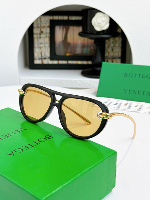 Sunglasses with black frame and gold-tone accents, amber-tinted lenses.