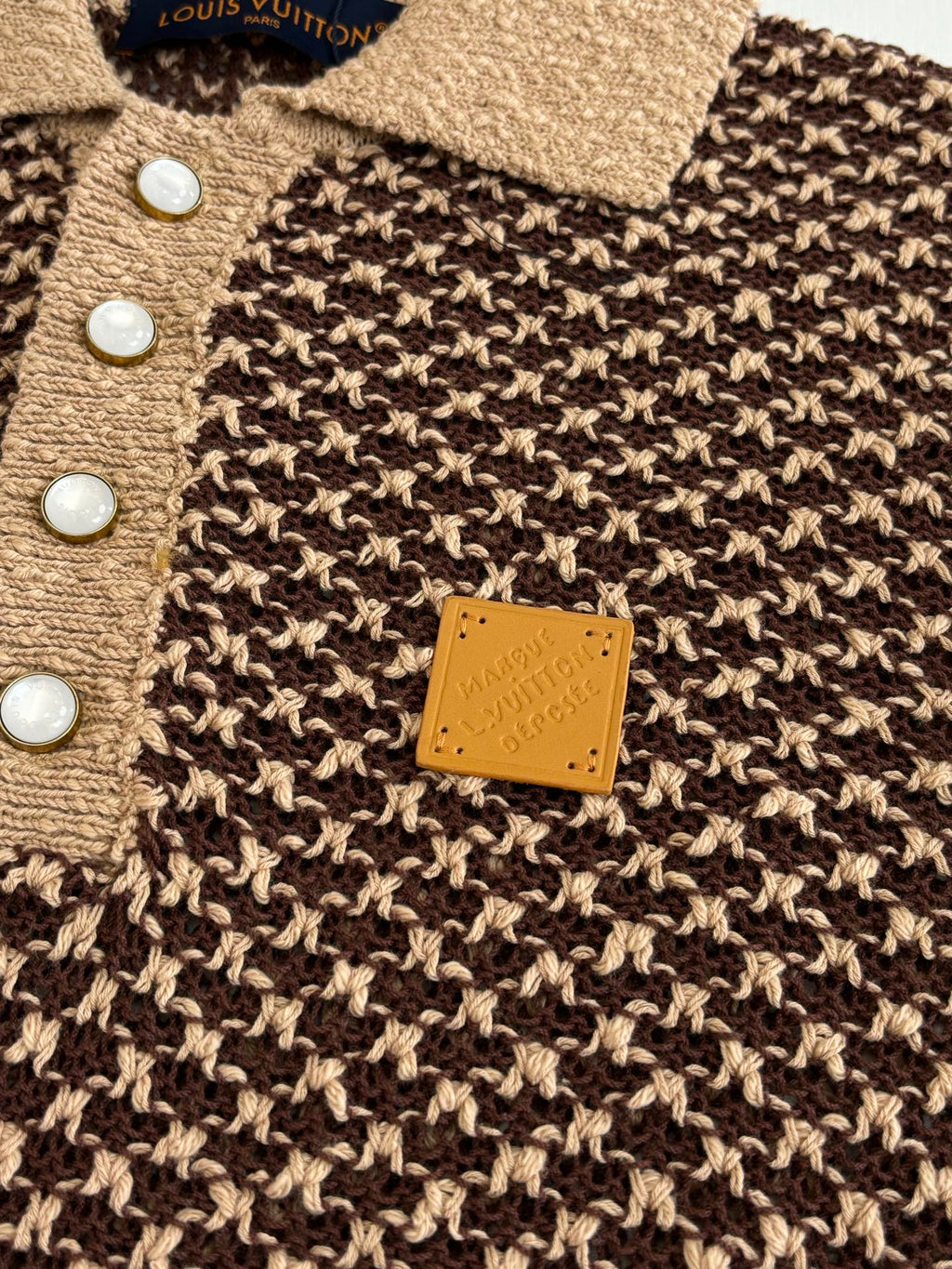 Knit polo shirt close-up with tan button placket and small rectangular logo patch