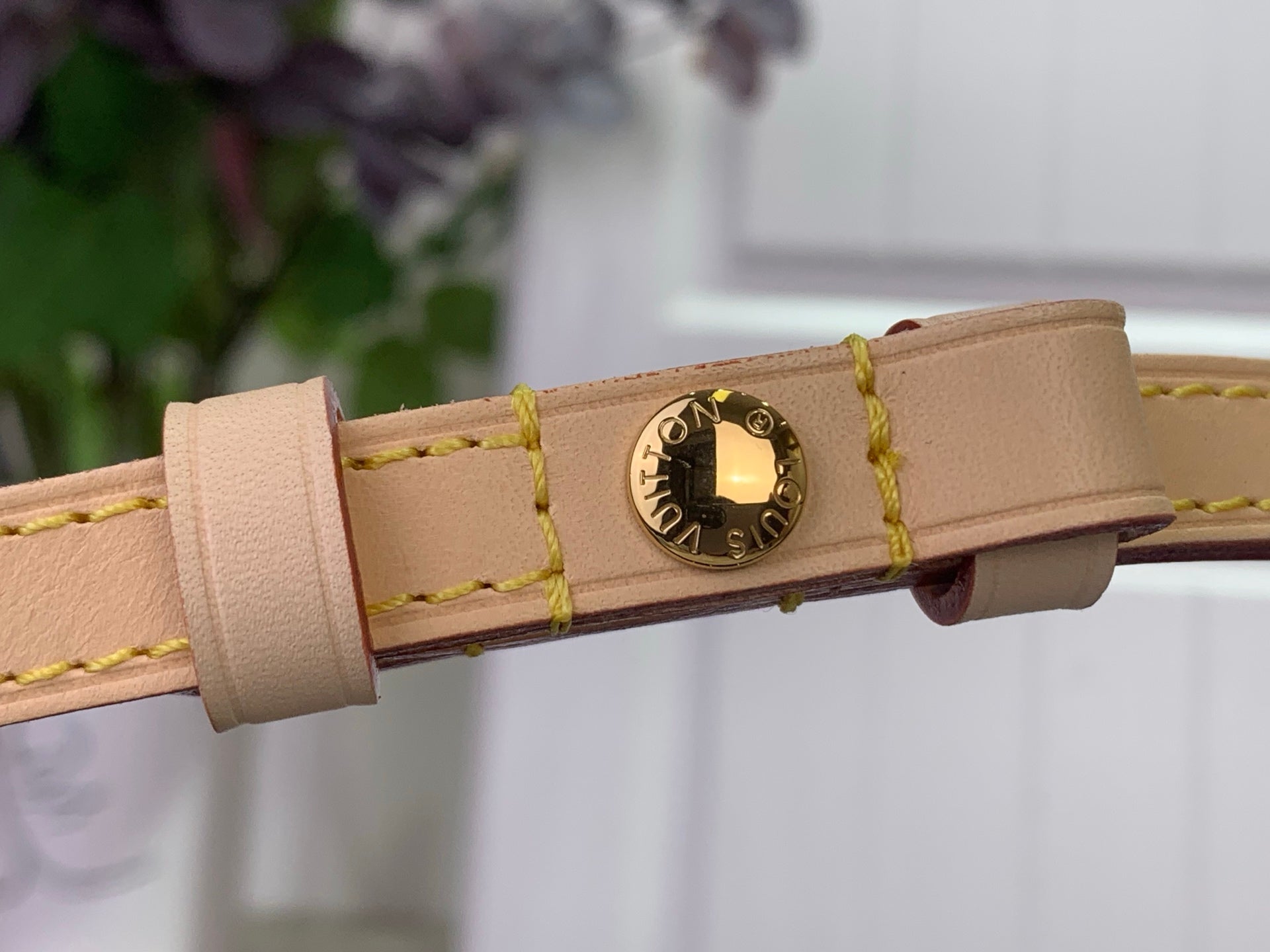 Beige leather strap end with gold-tone clasp on a Louis Vuitton crossbody bag
