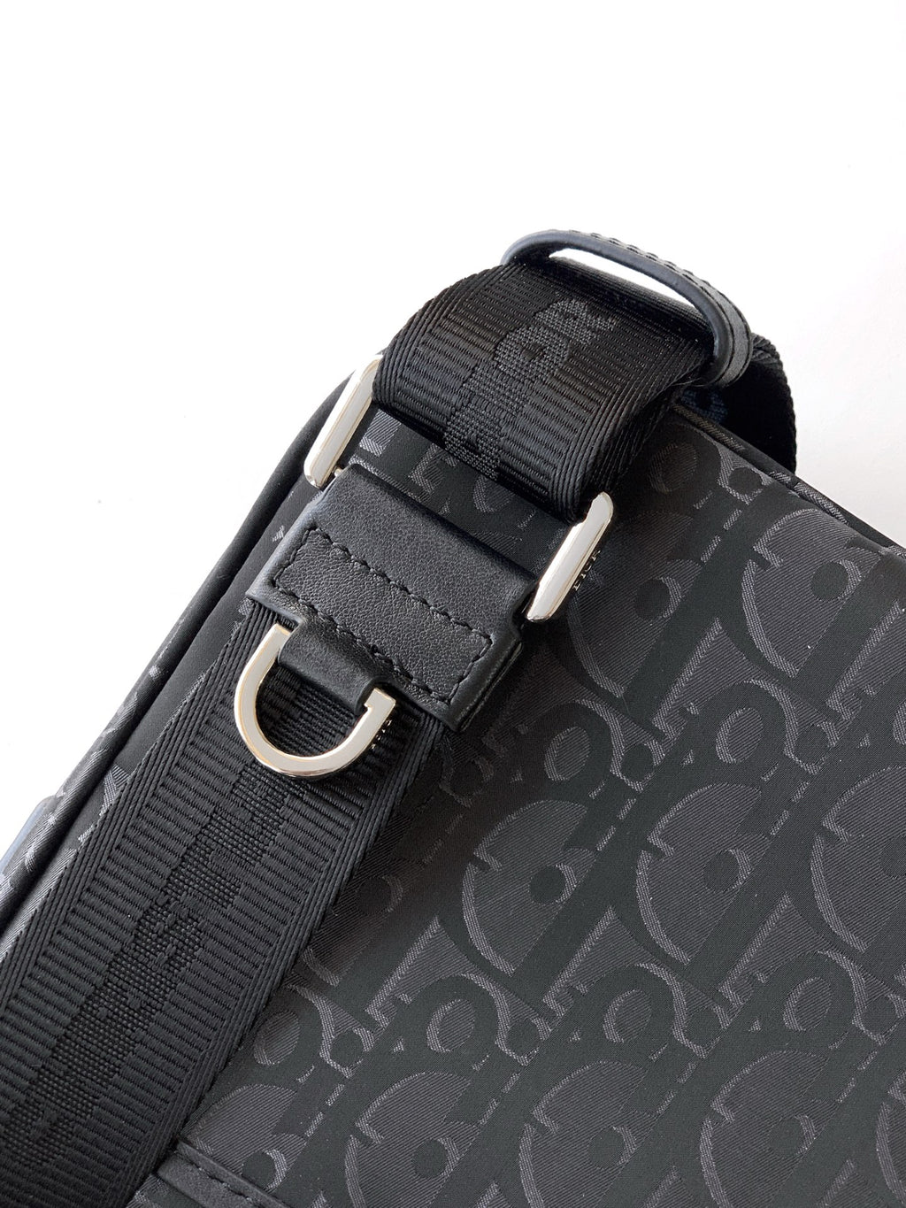 Dior bag strap close-up with black webbing, metal buckle, and dark Oblique pattern