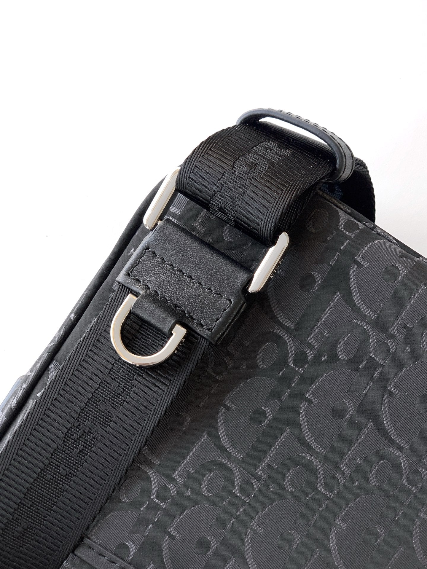 Dior bag strap close-up with black webbing, metal buckle, and dark Oblique pattern