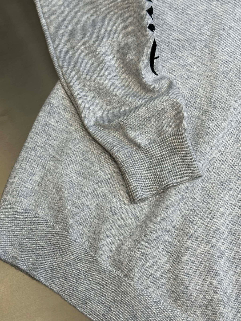 Light gray heather sweatshirt sleeve with black graphic detail near the cuff