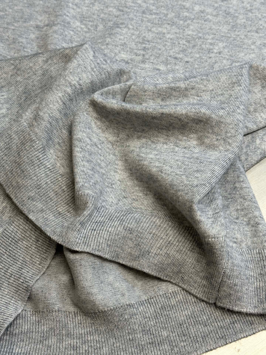 Light gray heather sweatshirt folded with ribbed collar and cuffs visible