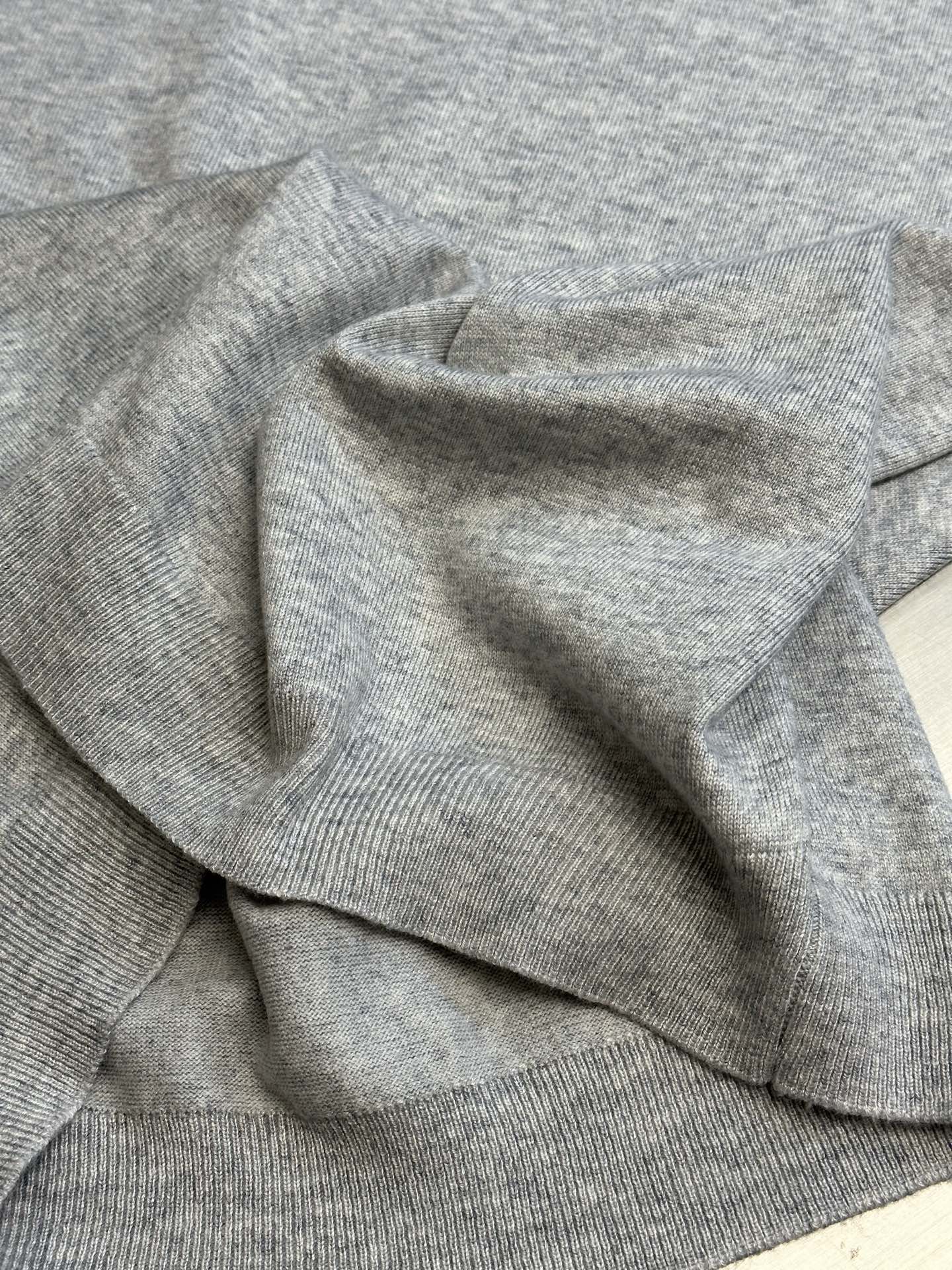 Light gray heather sweatshirt folded with ribbed collar and cuffs visible