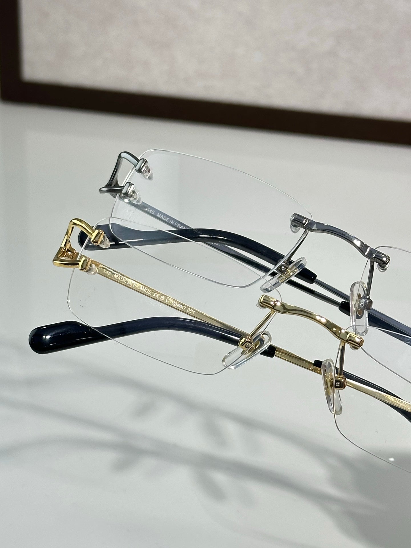 Two eyeglass frames: silver-tone and gold-tone with clear lenses and dark temple tips