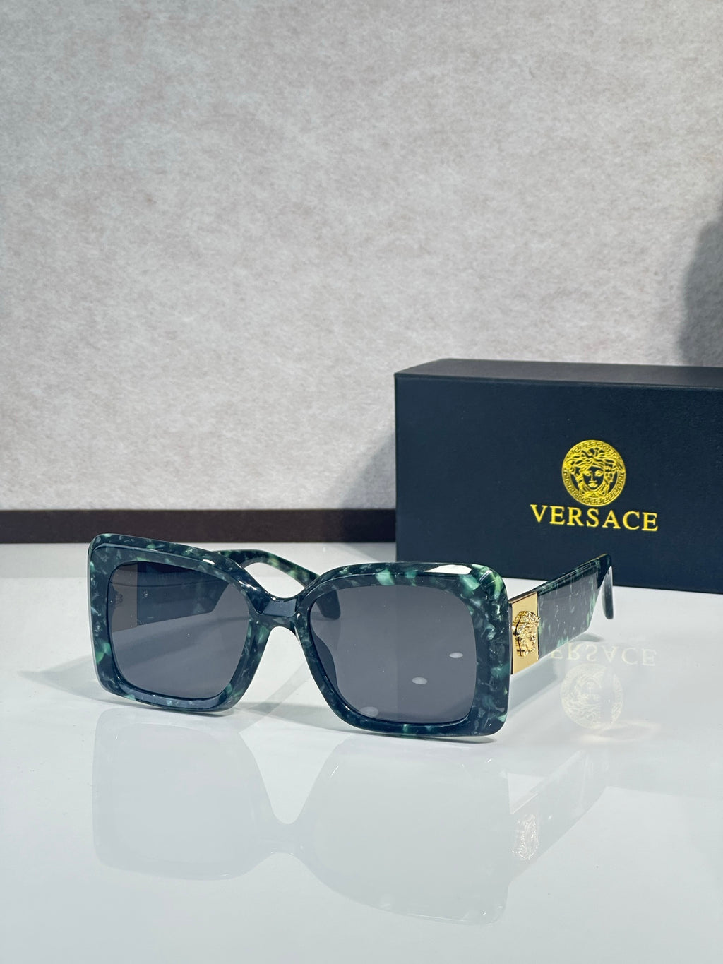 Square Versace sunglasses, teal-blue frame with dark gray lenses.