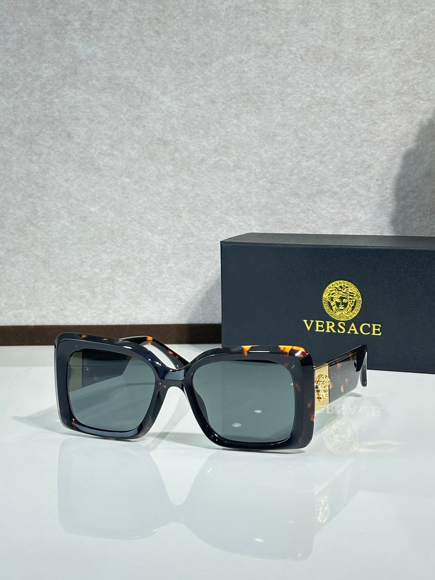 Square Versace sunglasses, black frame with teal-tinted lenses.