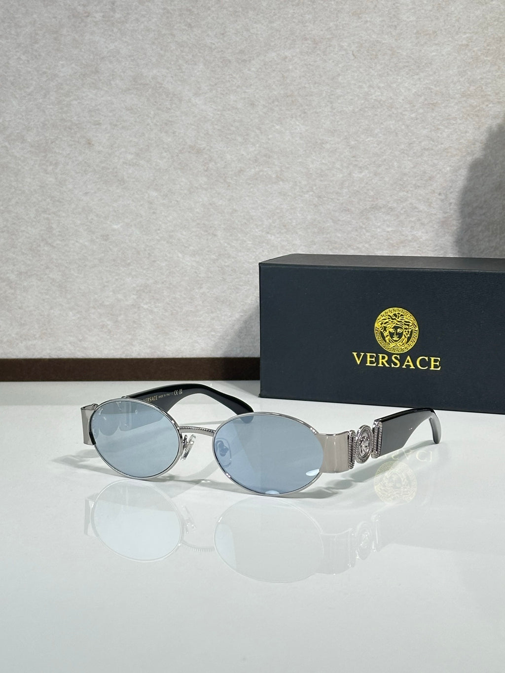 Oval sunglasses with light blue lenses, silver-toned frame, gold logo hardware.