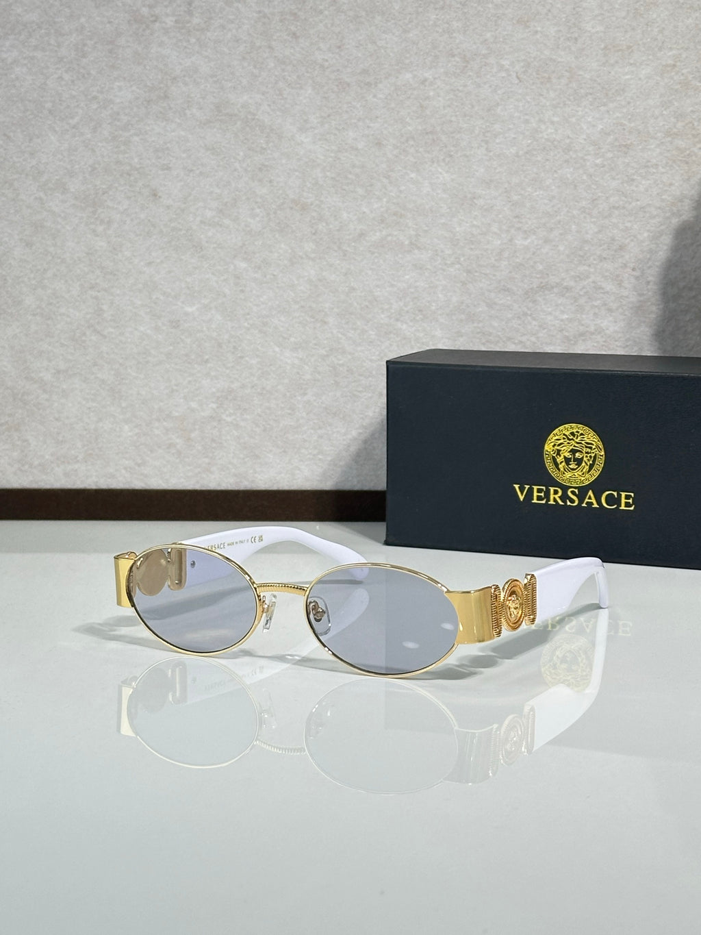 Oval sunglasses with gray-tinted lenses, gold temple details, clear lens tint.