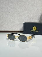 Oval sunglasses with dark gray lenses, gold temple details, black-and-gold frame.