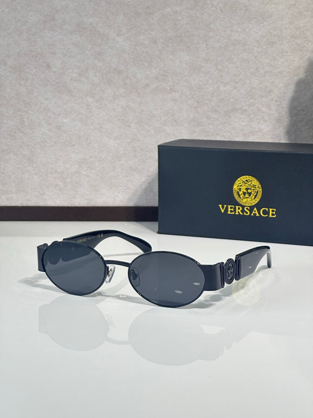 Oval sunglasses with dark blue lenses, black frame, gold temple details.