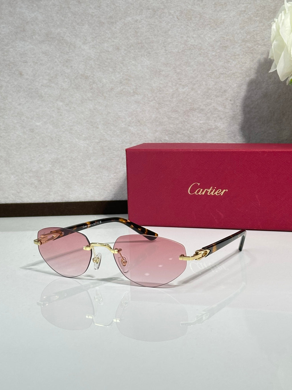 Cartier sunglasses with pink-tinted lenses, gold frame, and dark blue arms
