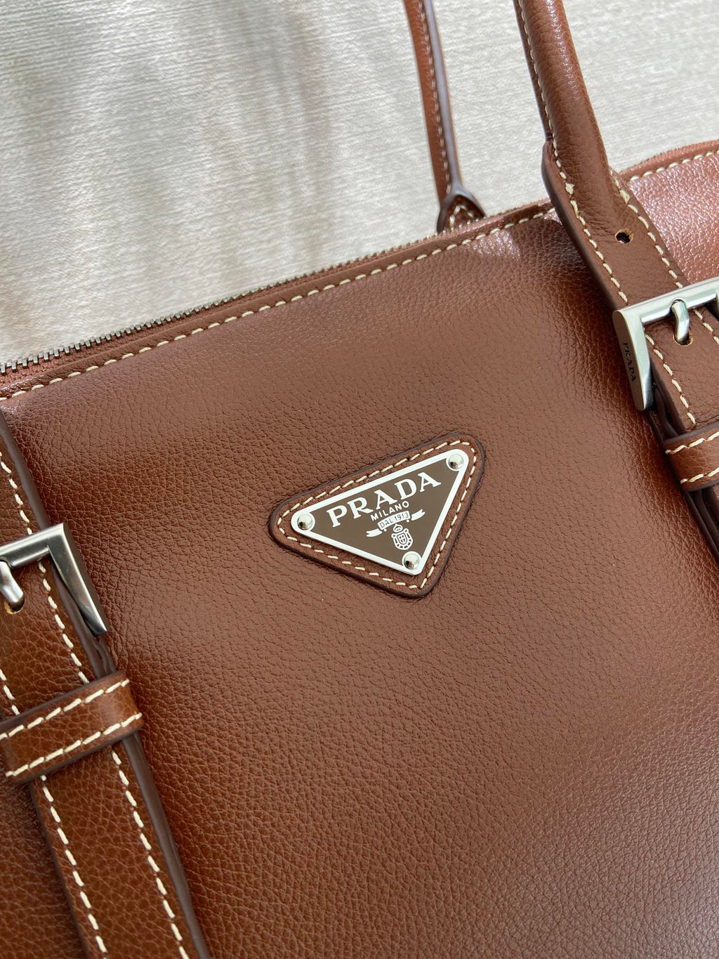 Prada logo triangle leather patch on brown bag with stitched trim and metal hardware