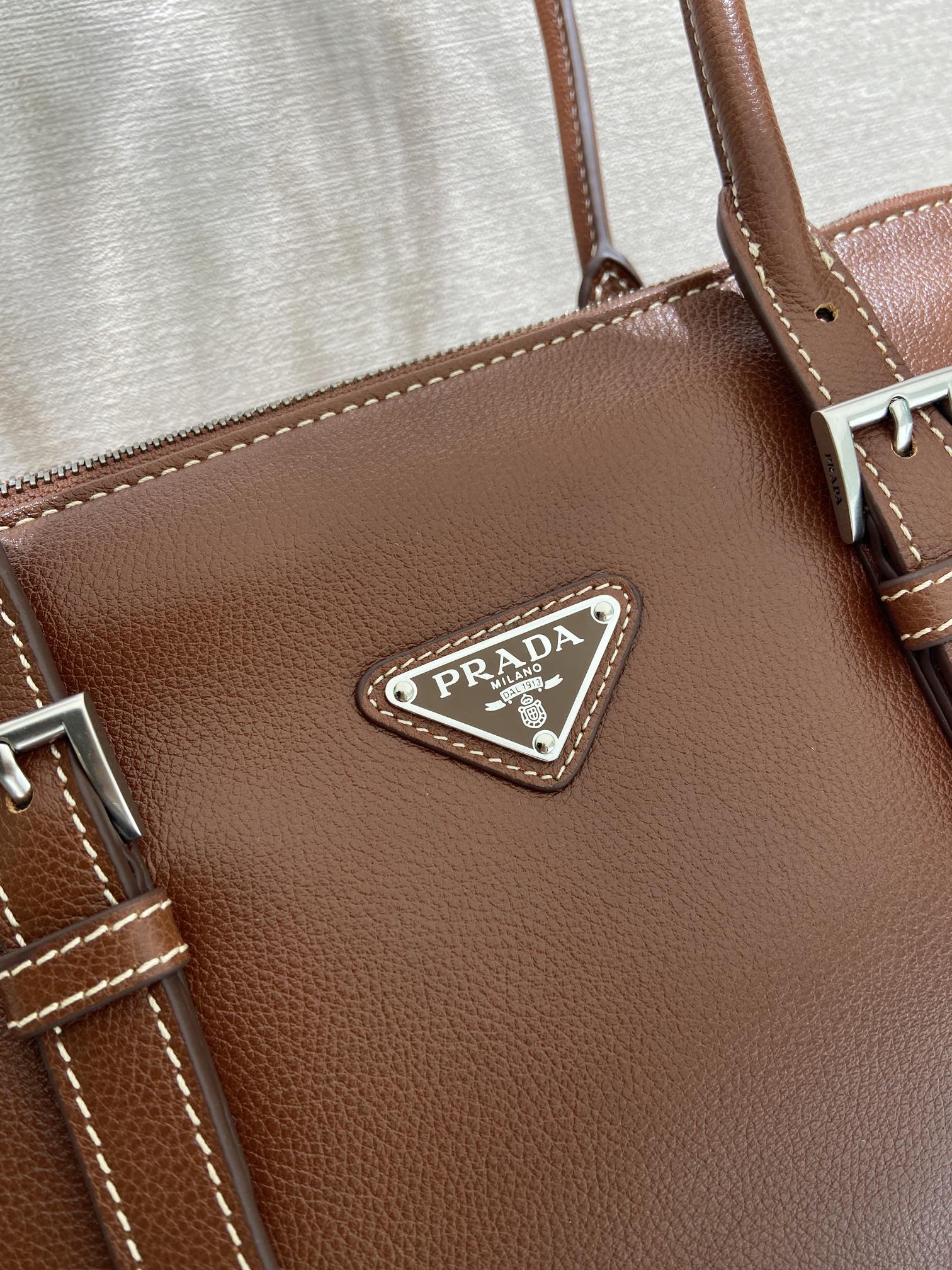 Prada logo triangle leather patch on brown bag with stitched trim and metal hardware