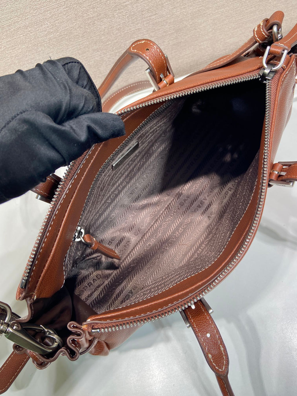 Prada brown leather zip-top bag open, showing patterned lining and zipper pull