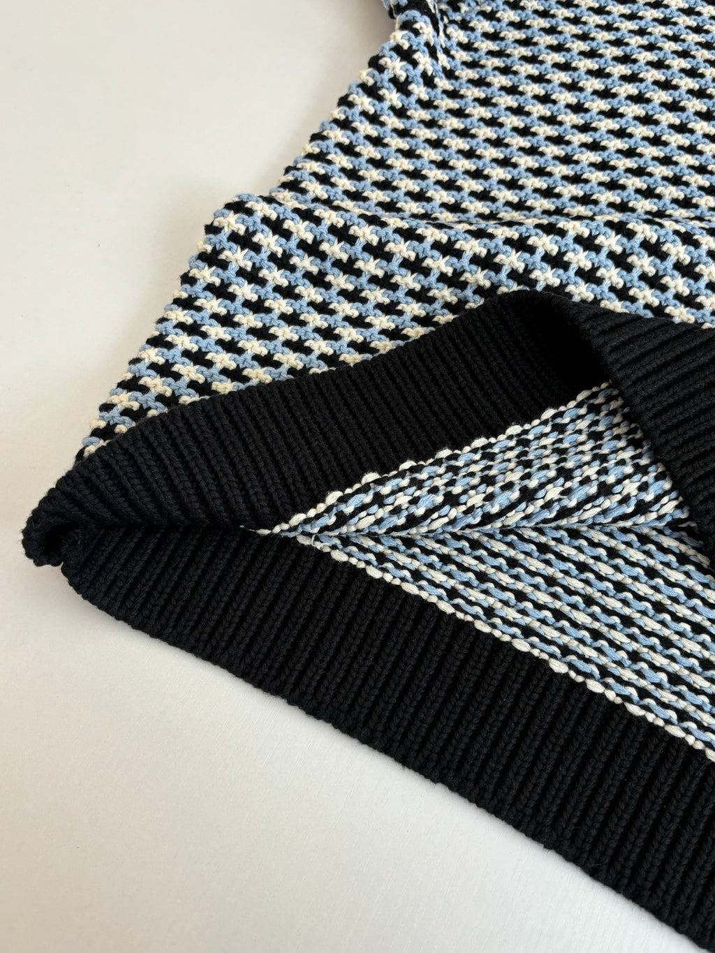 Houndstooth sweater hem detail, black ribbed trim with cream/blue check knit