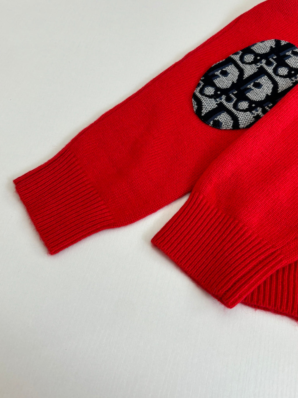 Red knit sweater sleeve with black-and-blue logo-pattern oval detail
