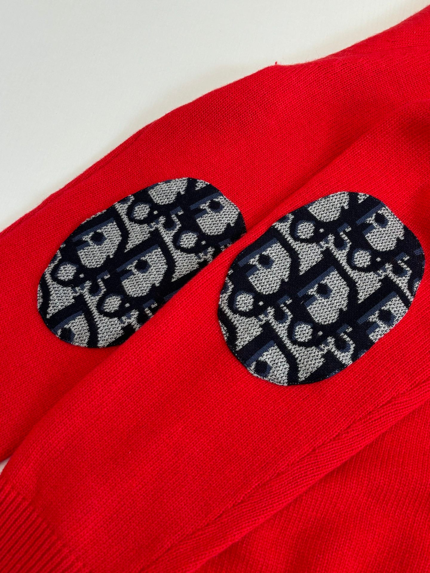 Red knit sweater sleeve with black-and-blue logo-pattern oval detail