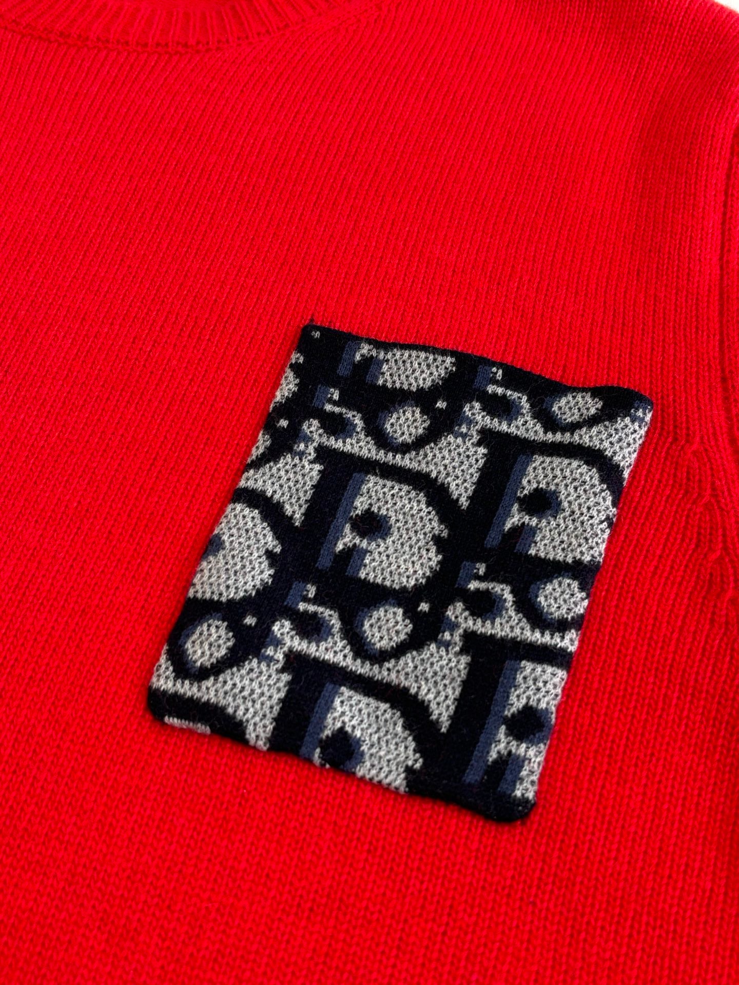 Red knit sweater with black-and-blue logo pattern patch on the chest