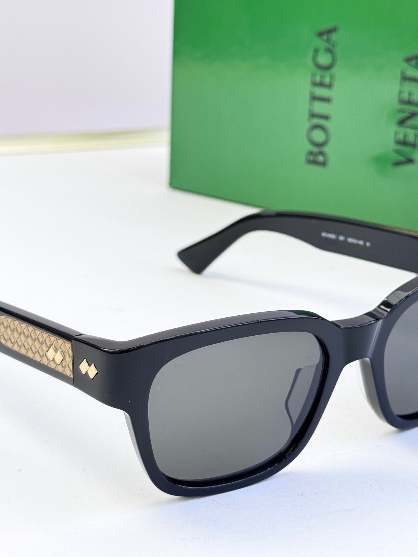 Bottega Veneta sunglasses close-up with dark frame and gold patterned temple