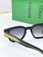Sunglasses with black frames, gold textured temple accents, and purple-tinted lenses