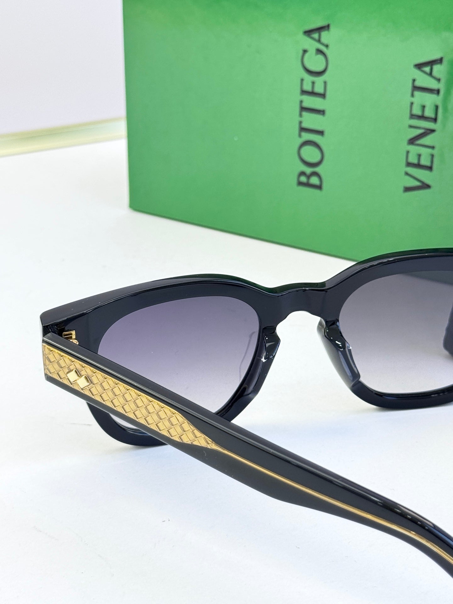 Sunglasses with black frames, gold textured temple accents, and purple-tinted lenses