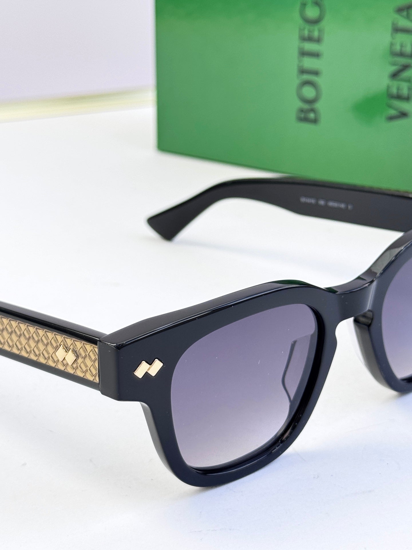 Black sunglasses close-up, textured gold temple detail and purple-tinted lenses
